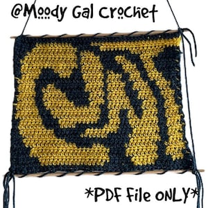 May include: A crocheted item featuring a swirling design in gold and navy blue. The text reads "@Moody Gal Crochet" and "*PDF File ONLY*". It is mounted on wooden dowels with hanging strings. The piece is a PDF file.
