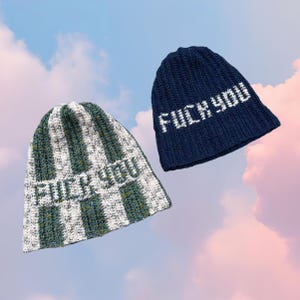 May include: Two knitted beanies. One is navy blue with white text that reads "FUCK YOU". The other is green and white striped with the same text. Both hats are displayed against a sky background.