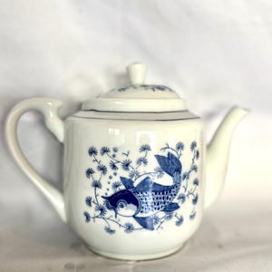 Könnte beinhalten: Weiße Teekanne mit einem blauen und weißen Blumendesign mit einem Fisch. Die Teekanne hat einen Deckel und einen Henkel.