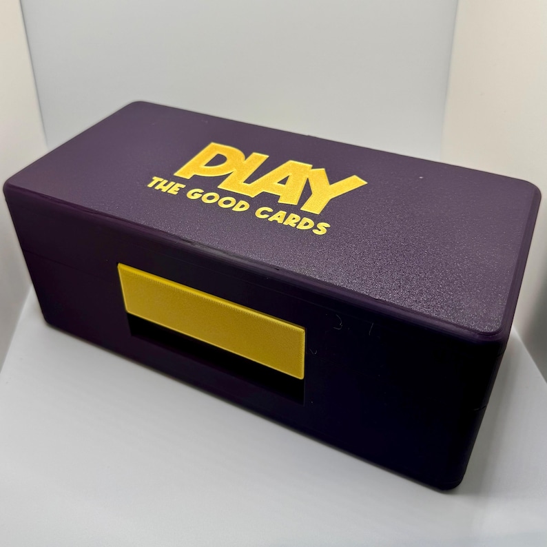 May include: A purple box with a gold "PLAY THE GOOD CARDS" logo. The box has a yellow latch.