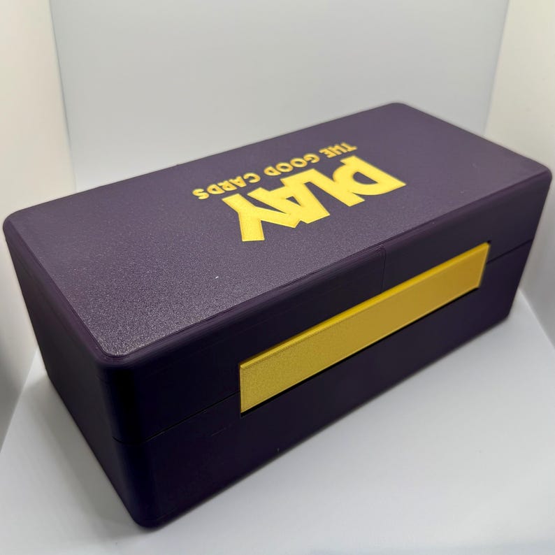 May include: A purple box with a gold sliding lid. The box has the text "Play The Good Cards" printed on the top in gold letters.