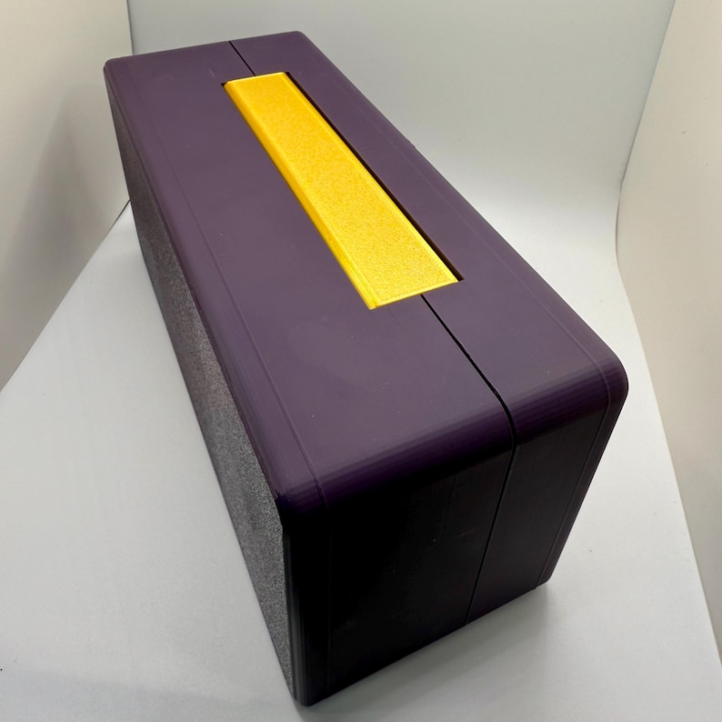 May include: A purple rectangular box with a yellow rectangular panel on the top. The box has a textured surface.