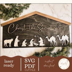 May include: Wooden nativity scene with the text "Christ the Savior is born." The scene features laser-cut figures of the nativity, including a cow, wise men, and camels. The background is dark with a wooden frame.