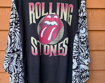May include: A black long-sleeve shirt featuring the Rolling Stones logo with a red tongue and lips graphic. The text Rolling Stones is printed in a distressed font. The sleeves are made of a contrasting white and black paisley patterned fabric.