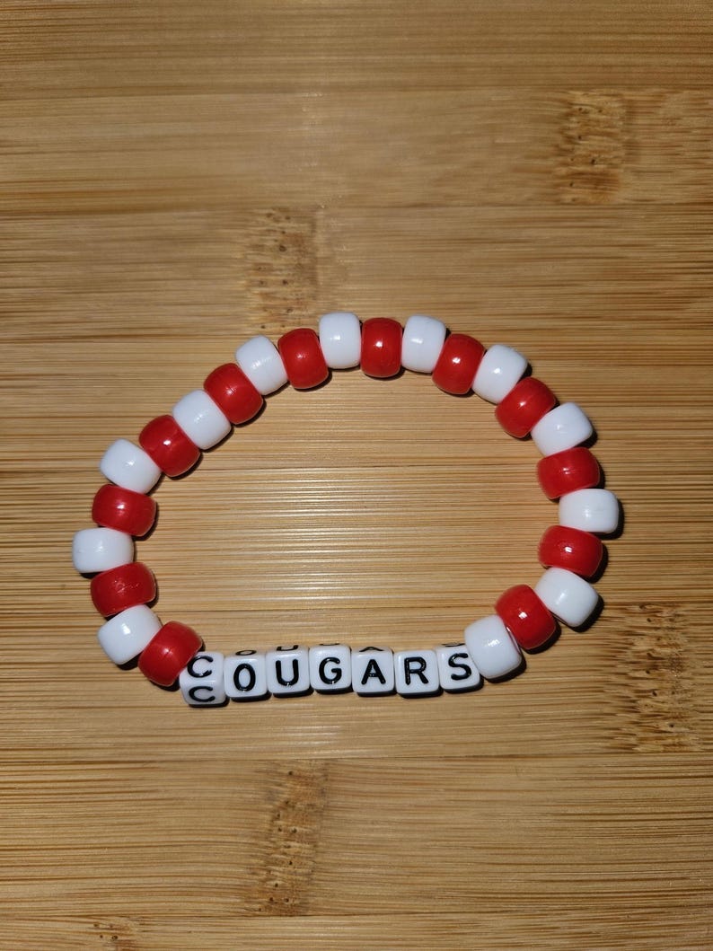 May include: Red and white beaded bracelet with the word "COUGARS" spelled out in black letter beads.
