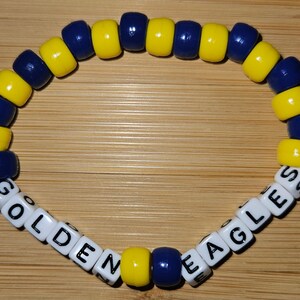 May include: A yellow and blue beaded bracelet with white letter beads spelling "GOLDEN EAGLES".