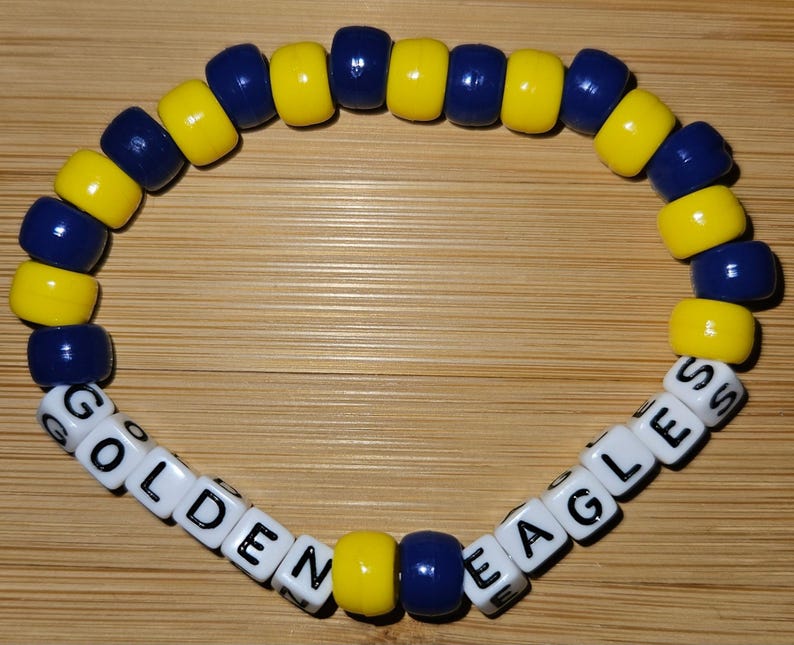 May include: A yellow and blue beaded bracelet with white letter beads spelling "GOLDEN EAGLES".