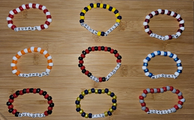 May include: Nine colorful beaded bracelets with white letter beads spelling out team names, including "Cougar", "Golden Eagles", "Texas A&M", "Longhorns", "Red Raiders", "Wildcats", "Bulldogs", "ETSU", and "Buckeyes".