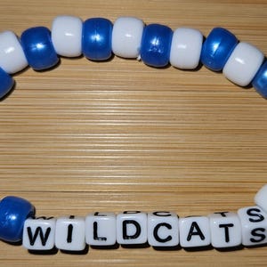 May include: A blue and white beaded bracelet with the word "WILDCATS" spelled out in black letters on white beads.