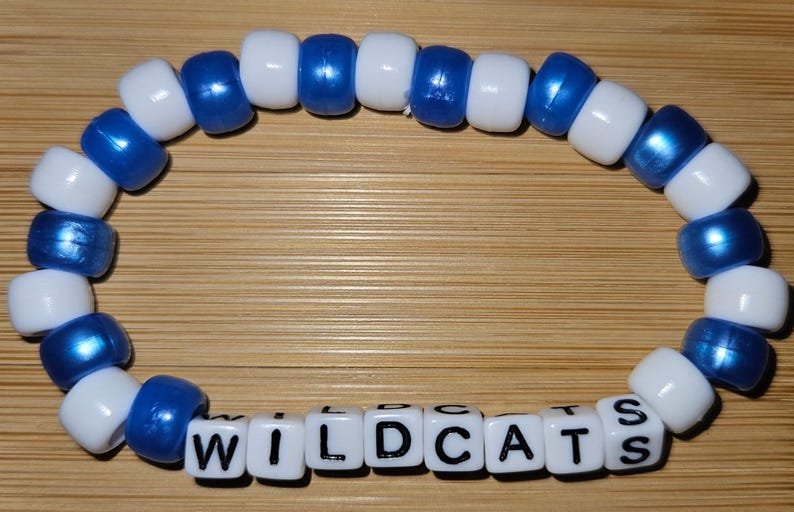 May include: A blue and white beaded bracelet with the word "WILDCATS" spelled out in black letters on white beads.