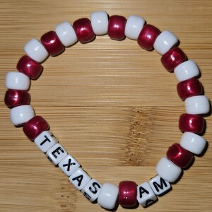 May include: A white and maroon beaded bracelet with the words "TEXAS A&M" spelled out in black letters on white beads.