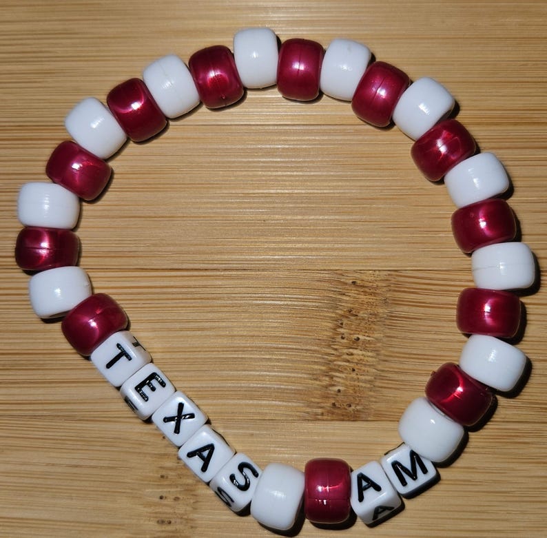 May include: A white and maroon beaded bracelet with the words "TEXAS A&M" spelled out in black letters on white beads.