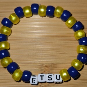 May include: A blue and yellow beaded bracelet with the word "ETSU" spelled out in white letter beads.