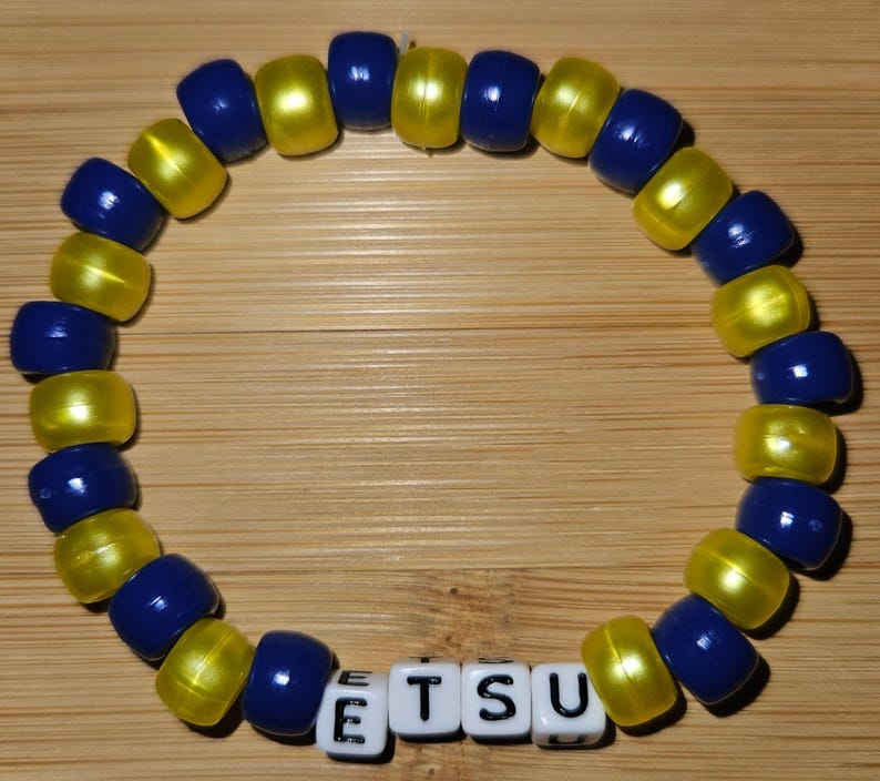 May include: A blue and yellow beaded bracelet with the word "ETSU" spelled out in white letter beads.