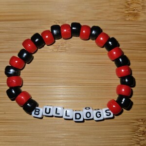 May include: A red and black beaded bracelet with the word "BULLDOGS" spelled out in white letter beads.