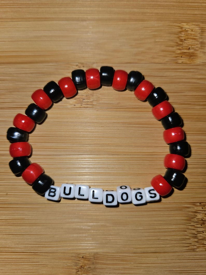 May include: A red and black beaded bracelet with the word "BULLDOGS" spelled out in white letter beads.