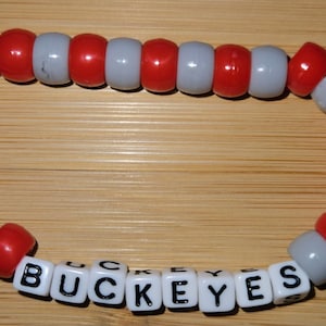 May include: A red and white beaded bracelet with the word "BUCKEYES" spelled out in black letters on white beads.