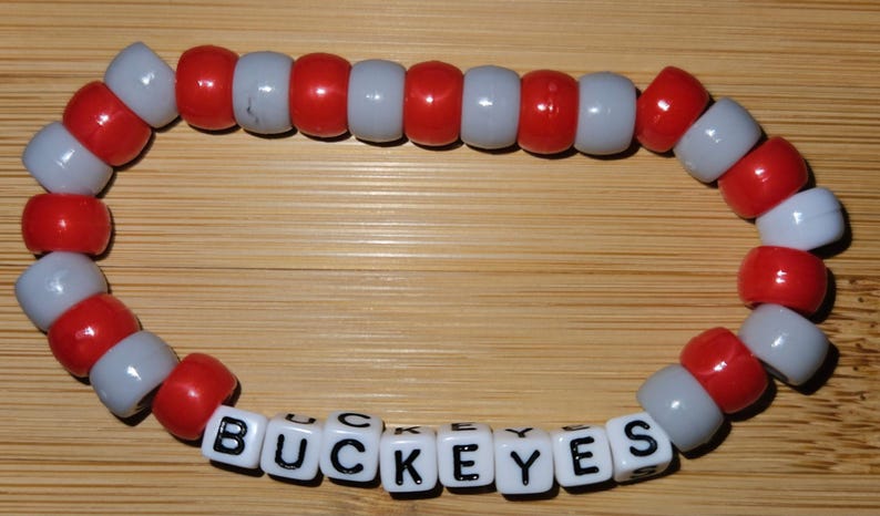 May include: A red and white beaded bracelet with the word "BUCKEYES" spelled out in black letters on white beads.