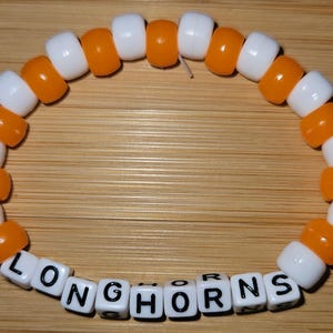 May include: Orange and white beaded bracelet with the word "Longhorns" spelled out in black letters on the white beads.