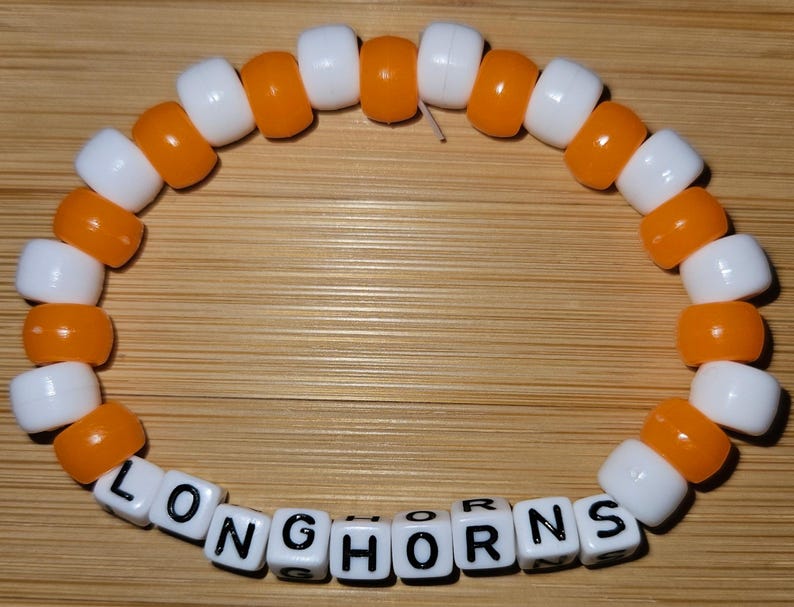 May include: Orange and white beaded bracelet with the word "Longhorns" spelled out in black letters on the white beads.