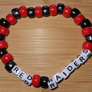 May include: Red and black beaded bracelet with white letter beads spelling "RED RAIDERS".