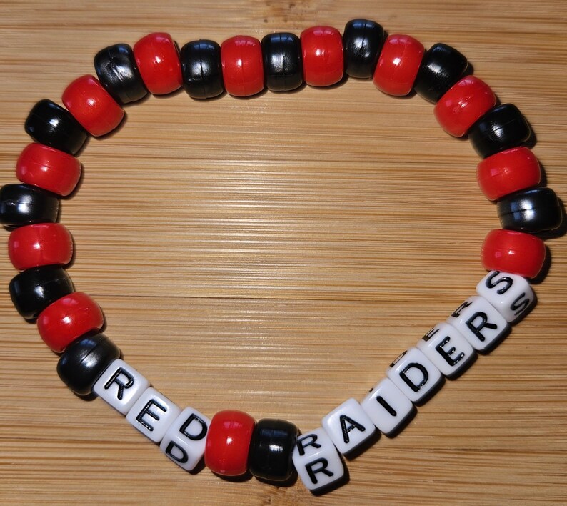 May include: Red and black beaded bracelet with white letter beads spelling "RED RAIDERS".