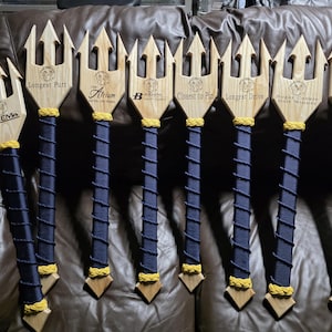 May include: Wooden golf-themed awards shaped like tridents. Each trident has a wooden head and a navy blue wrapped handle with gold accents. Text on the heads includes "Longest Putt", "Closest to Pin", and "Homebank".