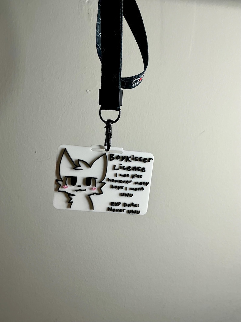 The Boykisser License attached to a black lanyard with a clip, hanging against a light wall, demonstrating the item's use as a badge or lanyard attachment.