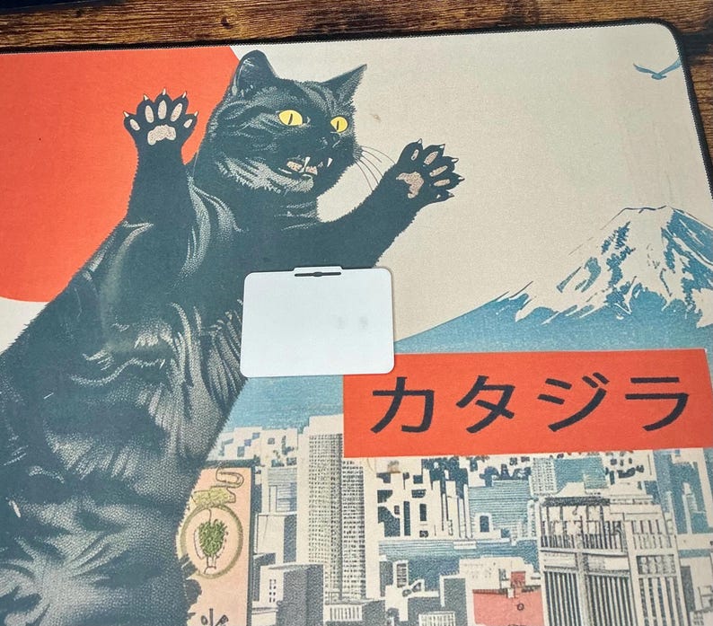 The back side of the white Boykisser License charm, resting on the Japanese-style desk mat with the black cat design.