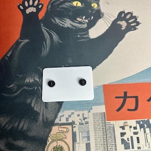 The back side of the white Boykisser License charm, resting on the Japanese-style desk mat with the black cat design.