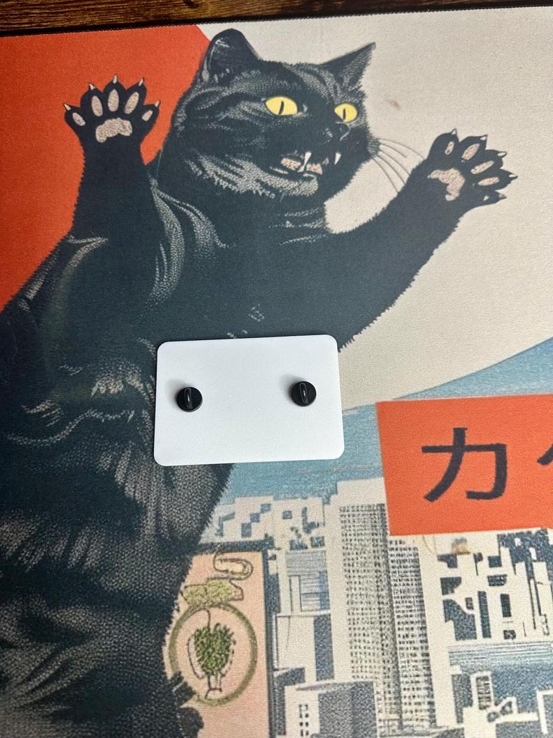 The back side of the white Boykisser License charm, resting on the Japanese-style desk mat with the black cat design.