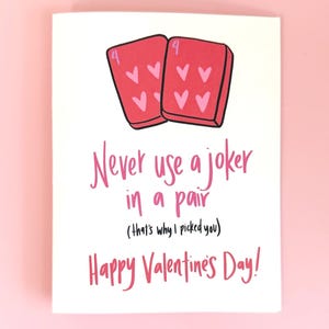 May include: Valentine's Day card with a pink background. The card features two red playing cards with heart symbols and the text "Never use a joker in a pair (that's why I picked you) Happy Valentine's Day!"