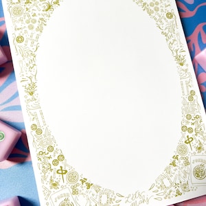 May include: A white paper with a gold border featuring Mahjong-themed illustrations and the words "Lets Mahj". The design includes various symbols and text elements associated with the game, with a blank oval space in the center.