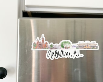 May include: A stainless steel refrigerator with a white cabinet above it. A sticker of a city skyline with the text "Auburn, AL" is on the refrigerator.