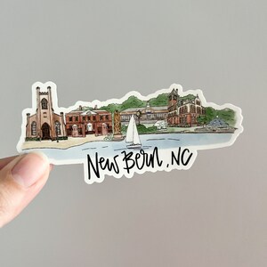 May include: A watercolor illustration of a New Bern, NC cityscape with a sailboat in the foreground. The illustration features a church, a brick building, and a building with a clock tower. The text "New Bern, NC" is written below the illustration.