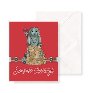 May include: A red Christmas card with a green and white illustration of a nutcracker dressed as a sea god. The nutcracker is holding a trident and standing on a rock with seaweed and sea creatures. The text "Sea side Greetings" is written in white cursive at the bottom of the card.