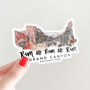 May include: A sticker with a watercolor illustration of a hiking trail in the Grand Canyon National Park. The text "Rim to Rim to Rim Grand Canyon National Park" is printed on the sticker.