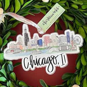 May include: A clear acrylic ornament featuring a watercolor illustration of the Chicago skyline. The ornament is decorated with the text "thirteenwhimsies" and "Chicago. II".