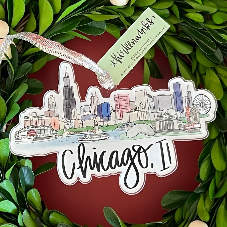 May include: A clear acrylic ornament featuring a watercolor illustration of the Chicago skyline. The ornament is decorated with the text "thirteenwhimsies" and "Chicago. II".