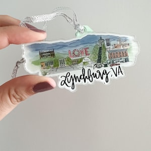 May include: A clear acrylic ornament featuring a watercolor illustration of a cityscape with the word "LOVE" in red letters and the text "Lynchburg, VA" in black script.