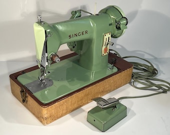 May include: A vintage mint green Singer sewing machine with a chrome needle bar and presser foot, mounted on a rectangular wooden base. The machine includes a matching mint green foot pedal connected by a long electrical cord and plug.