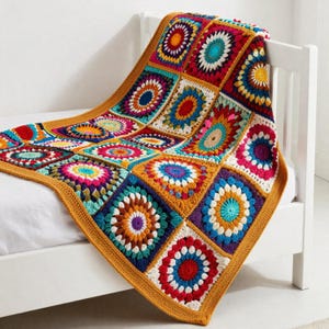 May include: A vibrant, hand-crocheted blanket with a patchwork design. The blanket is draped over a white bed frame. The squares are in shades of red, blue, yellow, and green, with a mustard yellow border. The blanket is made of yarn.