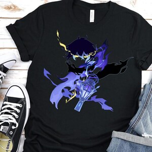 May include: Black t-shirt featuring a stylized illustration of a character with a lantern. The design incorporates shades of blue, purple, and yellow. The shirt is paired with black sneakers and denim shorts.