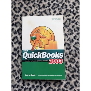 May include: A QuickBooks 2003 User's Guide. The cover features a gold and orange graphic of a person carrying a briefcase, with the QuickBooks logo and the text "Financial Software for Small Business."