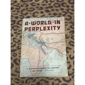 May include: A vintage book titled "A World in Perplexity" with a map illustration. The cover features red and black text, with a quote from President Wilson. The book is set against a patterned background.