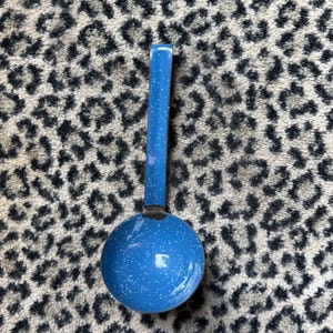 May include: A blue enamel ladle featuring a speckled white pattern throughout the surface. The kitchen utensil has a long, straight handle and a deep, circular bowl, showcasing a consistent blue finish with small white flecks across the entire piece.
