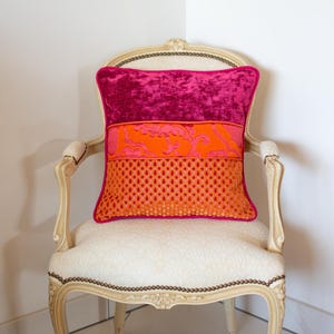 May include: A pink, orange and red patterned cushion on a white chair with ornate wooden arms.