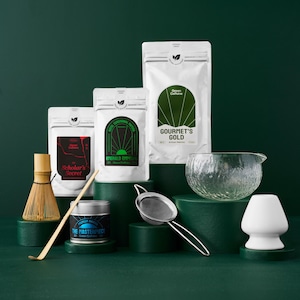 May include: A set of four matcha green tea powders, a bamboo whisk, a tea strainer, a tea bowl, and a teacup. The tea powders are labelled "Gourmet's Gold", "Emerald Emperor", "Scholar's Secret", and "The Masterpiece".