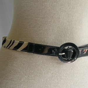 May include: A black patent leather belt with a zebra print fabric trim and a large round buckle.