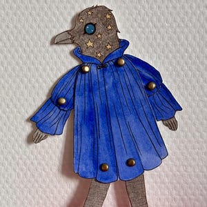May include: A whimsical paper cutout of a bird-like figure. The figure has a gray head adorned with gold stars and a blue eye. It wears a blue coat with gold buttons. The figure stands on a red surface.